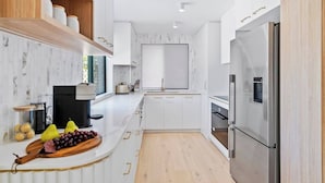 Cocina moderna con alacenas blancas, un refrigerador de acero inoxidable y una encimera de madera con frutas.