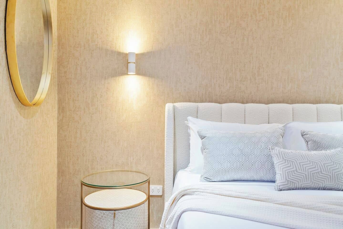 A neatly arranged bedroom with a bed, bedside tables, and a wall-mounted light fixture.