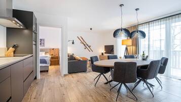 A modern kitchen with a built-in oven, a dining area with a round table and chairs, and a living area with a sofa and a ski rack on the wall.