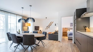 A modern kitchen with dark cabinets, a wooden dining table, and a chandelier. - Charming Apartment in Salzburg Without Deposit (Bad Hofgastein)