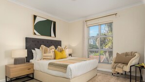 A bedroom with a bed, nightstands, a chair, a window with blinds, and a painting on the wall. - Villa Italia Getaway,  Pool, Gym, Netflix, Wifi (Cape Town)