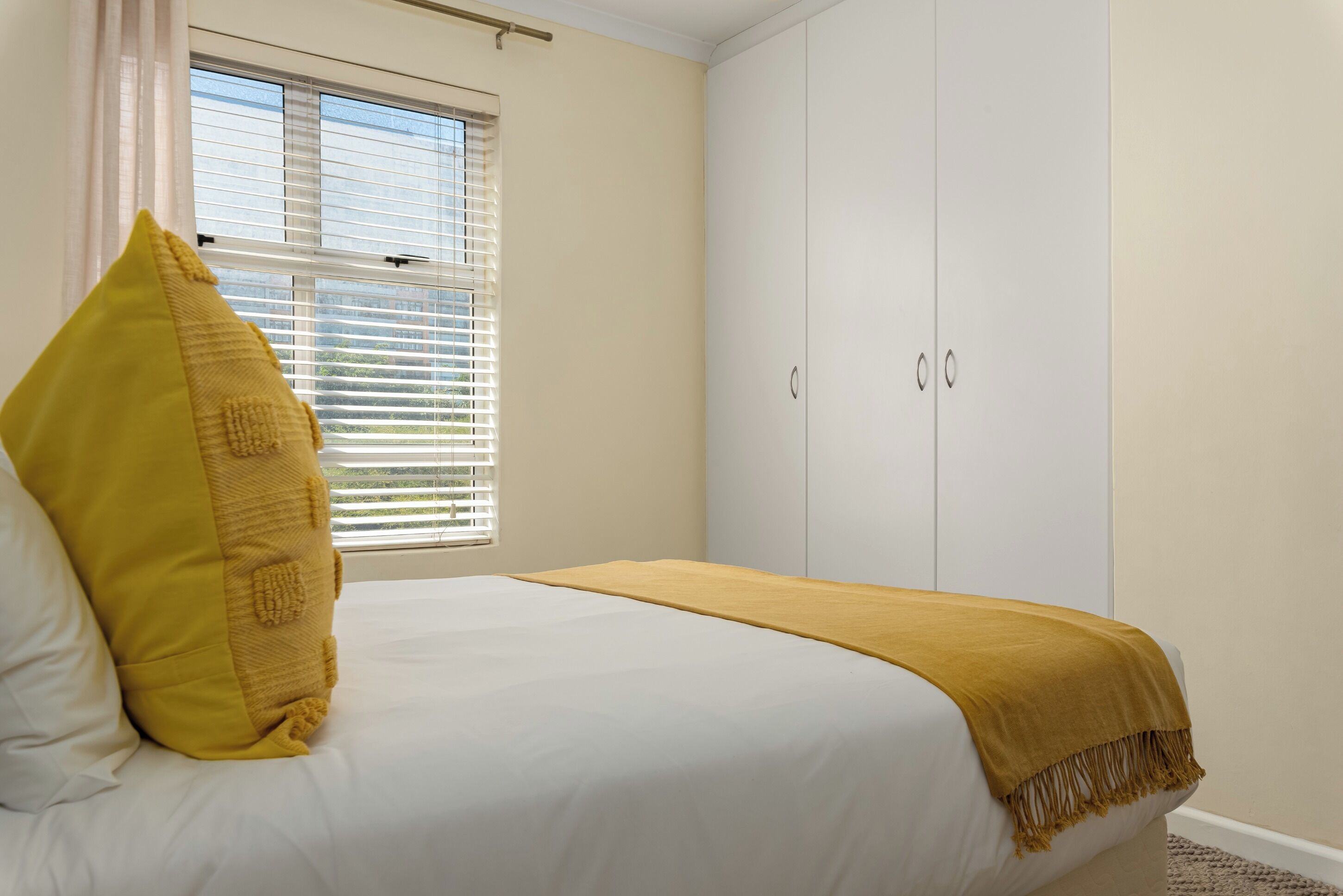 A bedroom with a bed, a window with blinds, and a wardrobe.