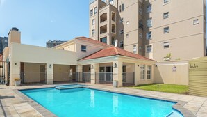 A swimming pool with a tiled deck, surrounded by a building with balconies and a covered patio area. - Villa Italia Getaway,  Pool, Gym, Netflix, Wifi (Cape Town)