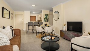 A living room with a sofa, a coffee table, a TV, and a dining area with chairs and a table. - Villa Italia Getaway,  Pool, Gym, Netflix, Wifi (Cape Town)