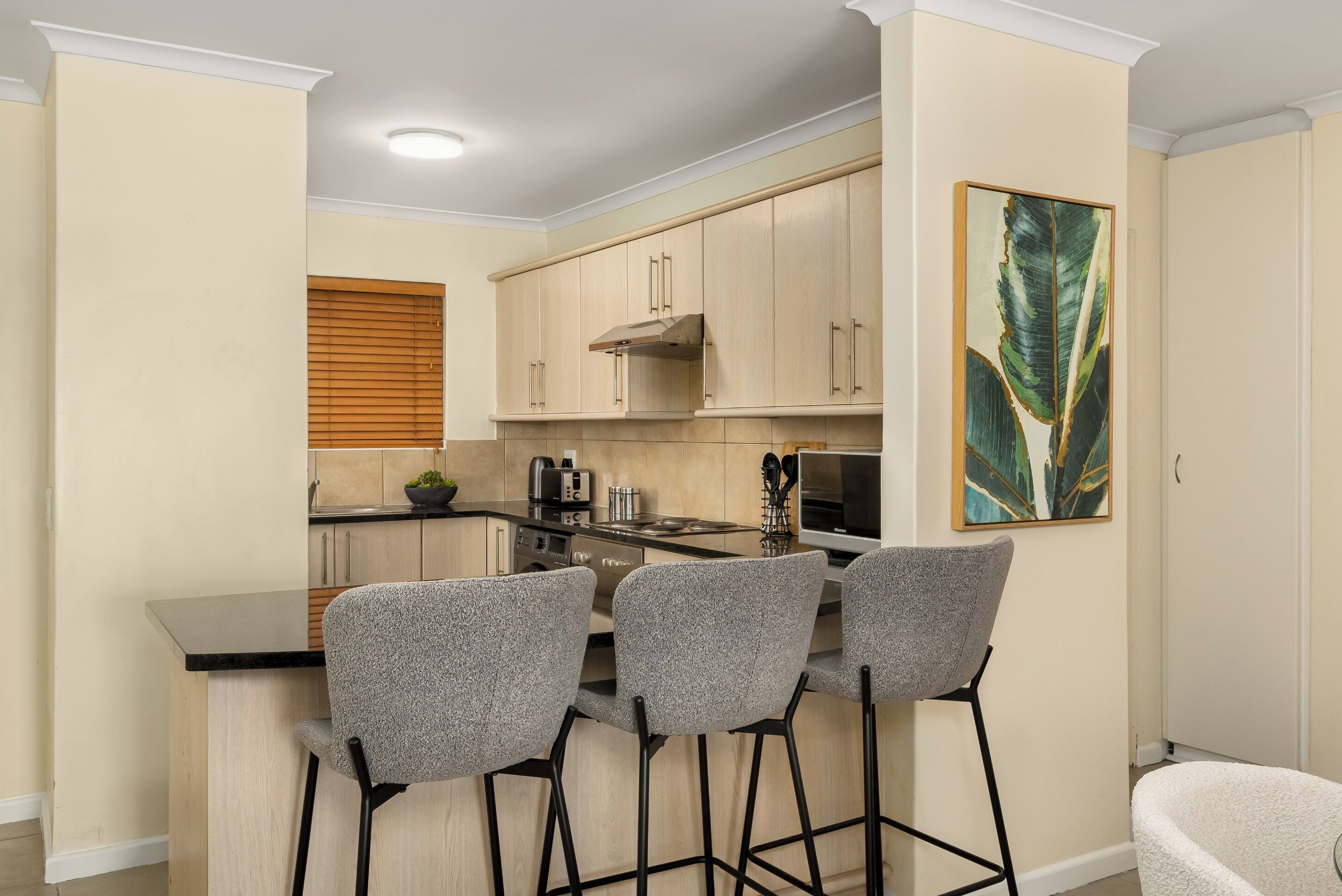A compact kitchen with a central island, bar stools, wooden cabinets, and a modern stove.