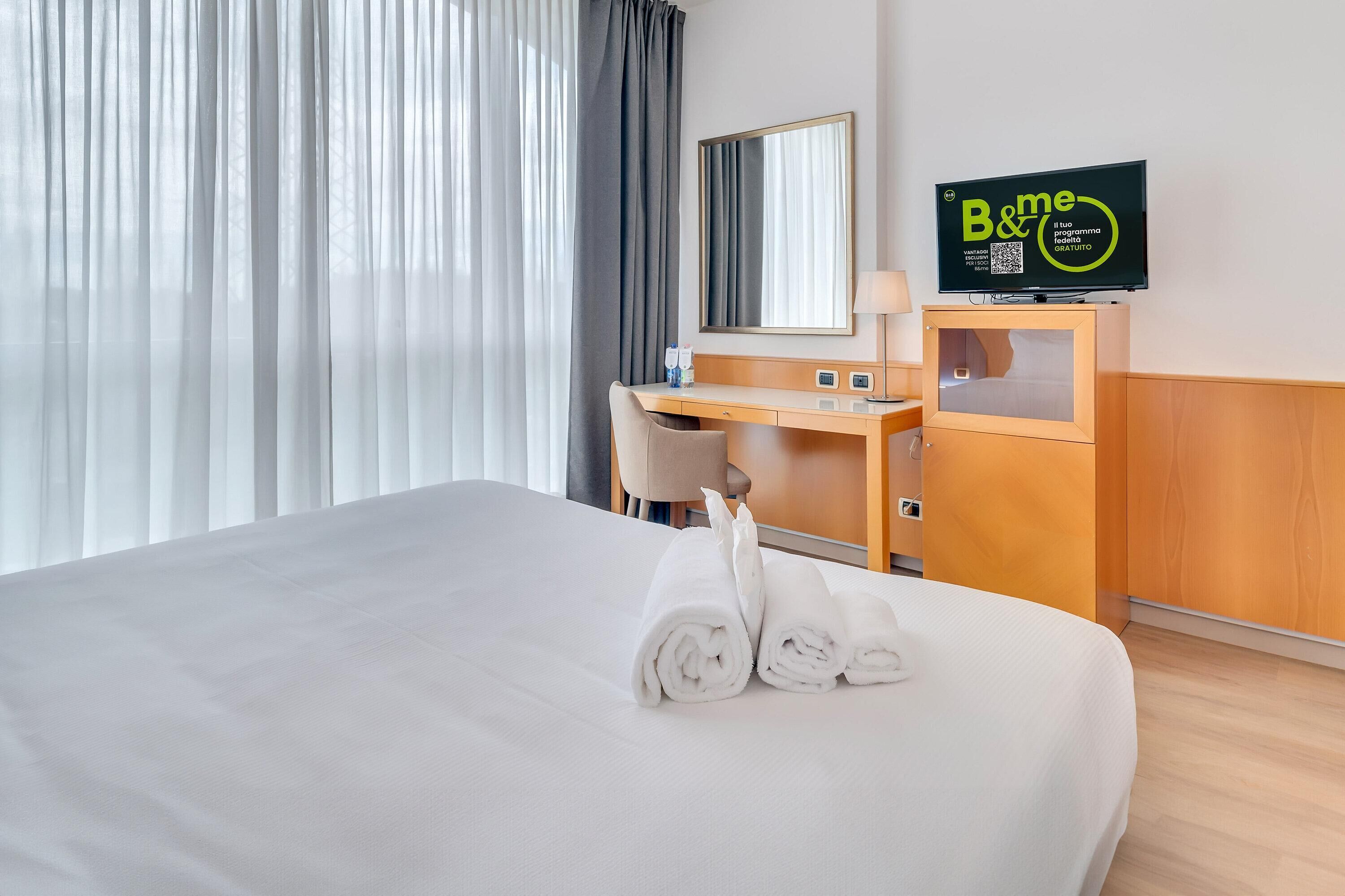 A hotel room with a bed, a desk, a chair, a TV, and a mirror.