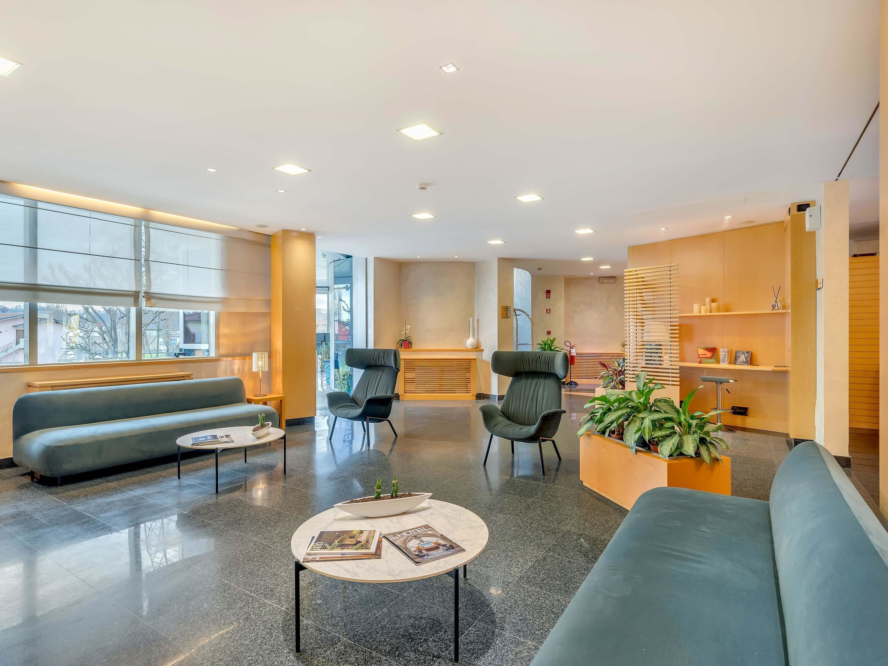 A modern hotel lobby with a blue sofa, a round table with magazines, a reception desk, and a staircase leading to an upper floor.
