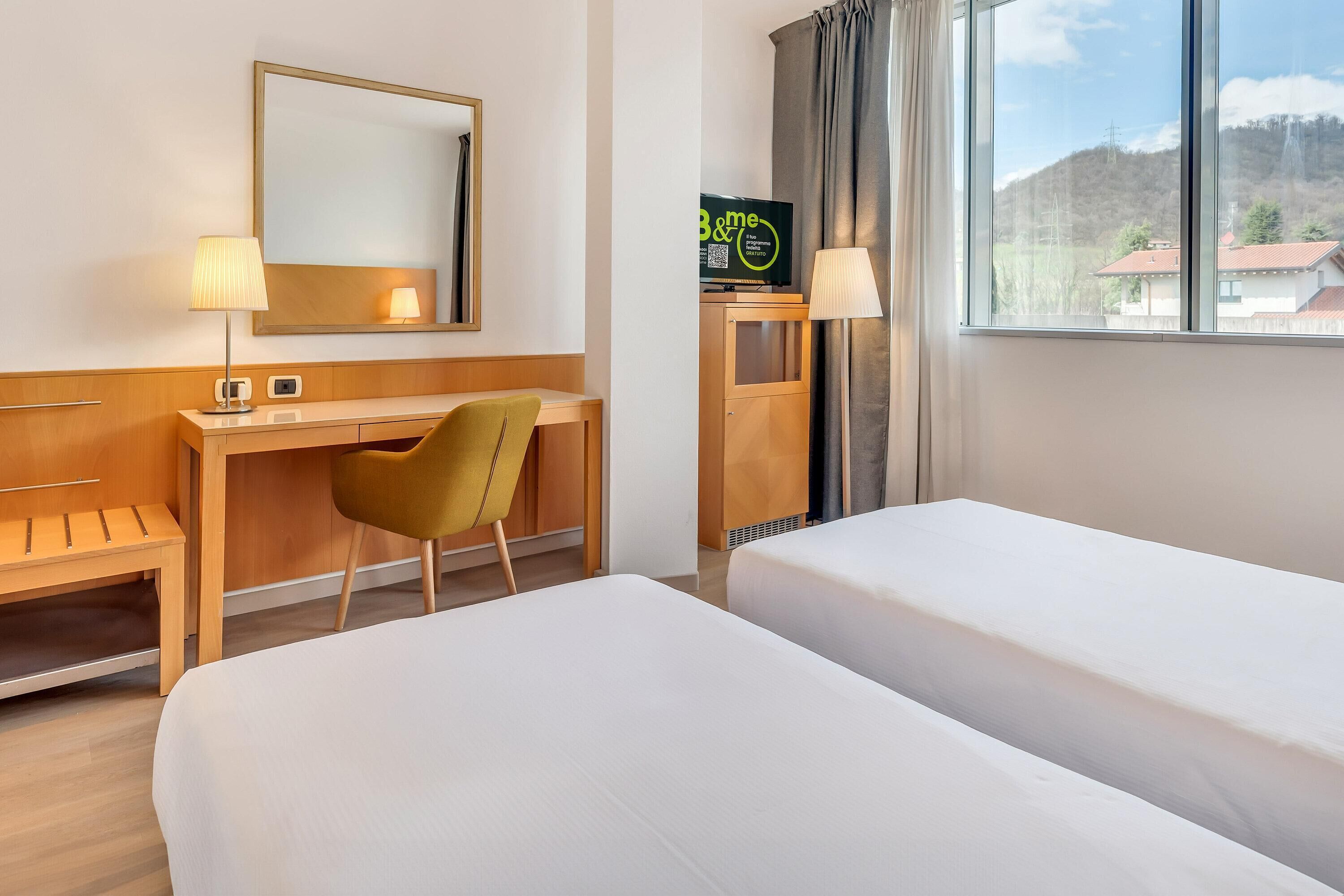 Une chambre d’hôtel équipée d’un lit, d’un bureau, d’une chaise, d’une télévision et d’une fenêtre donnant sur une vue sur la montagne.