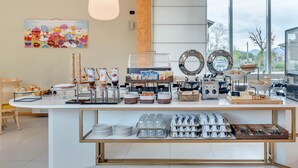 Un bufé de desayuno con diversas opciones de comida, una estación de café y un amplio ventanal con vistas al exterior.