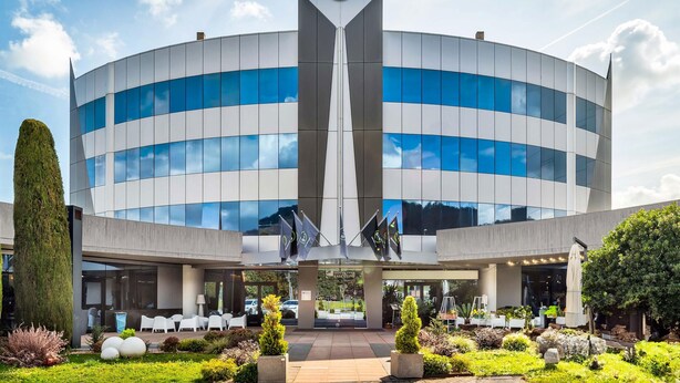 Un hotel B&B moderno con un atrio central, mobiliario exterior y jardines ajardinados.