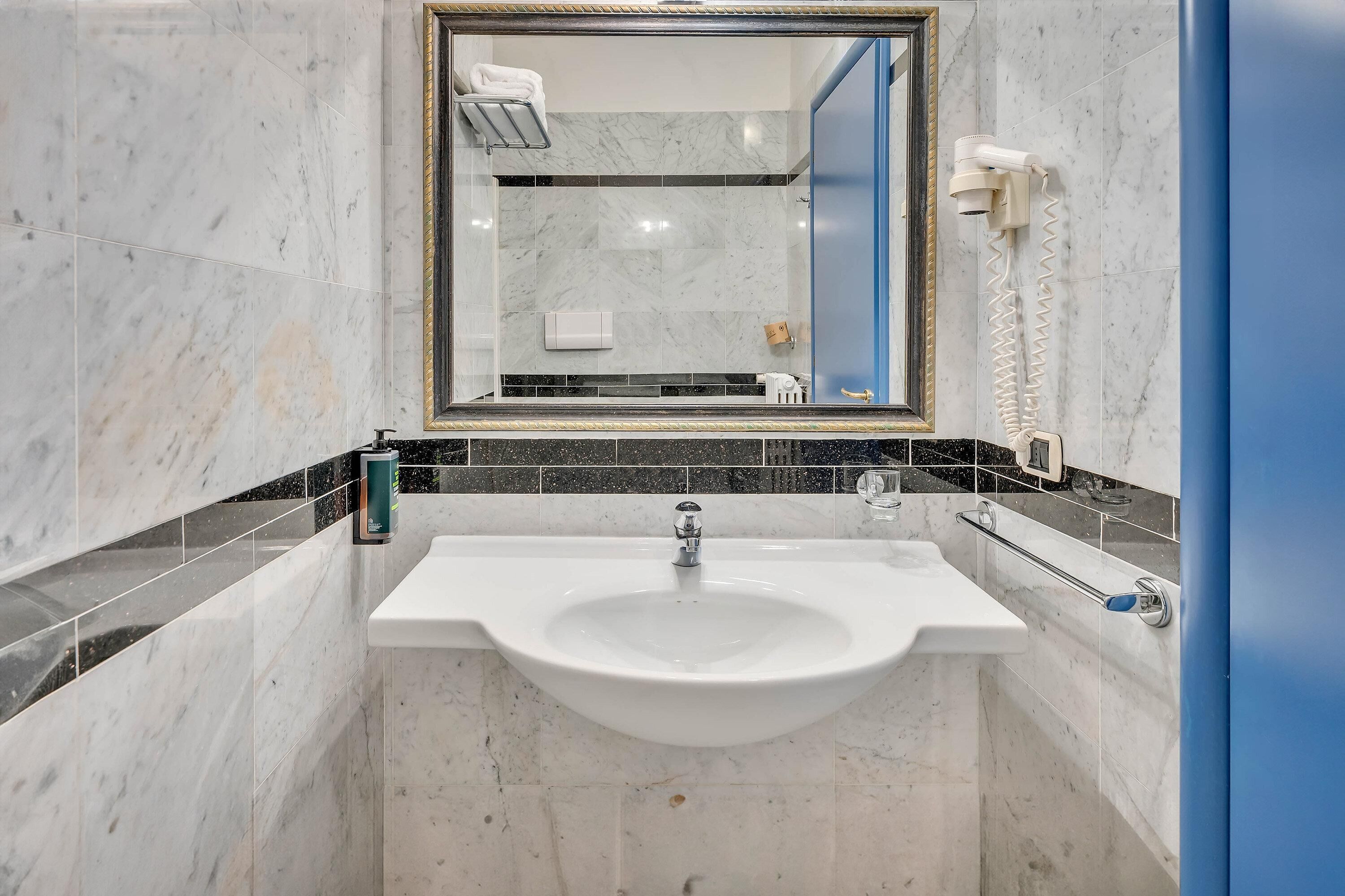 Un baño con un lavamanos blanco, un espejo y un secador de pelo en la pared.