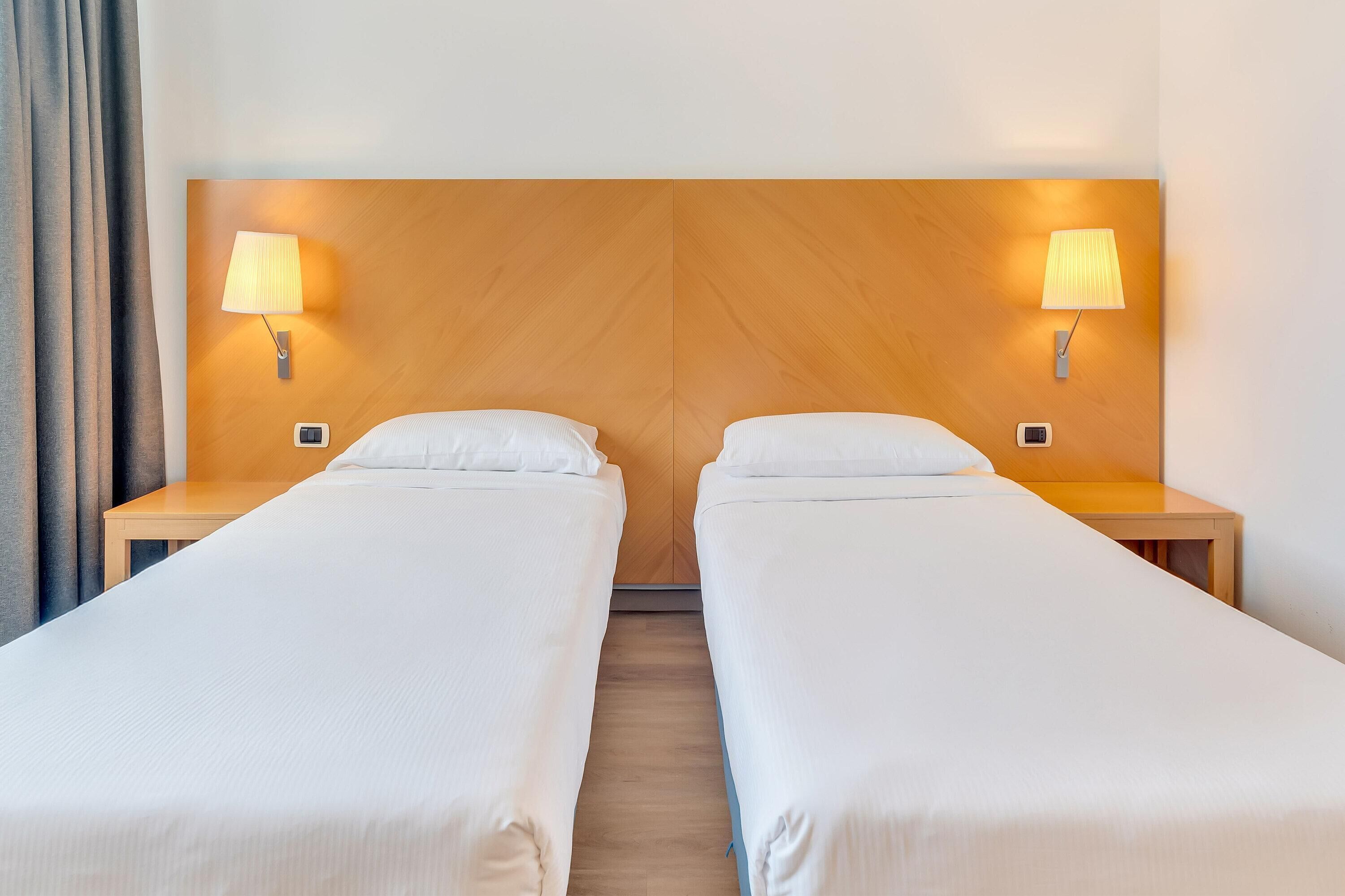 A double room with two beds, each with a nightstand and a wall-mounted lamp.