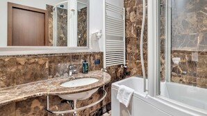 Un baño con lavamanos de mármol, bañera y cabina de ducha con paredes de vidrio.