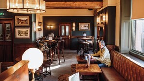 A cozy restaurant interior with wooden furniture, a large chandelier, and framed pictures on the walls. - Agricultural Inn (Penrith)