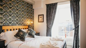 A neatly made bed with white linens, a patterned headboard, and a bedside table with a lamp. - Agricultural Inn (Penrith)