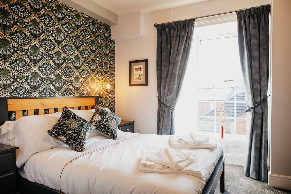 A neatly made bed with white linens, a patterned headboard, and a bedside table with a lamp.