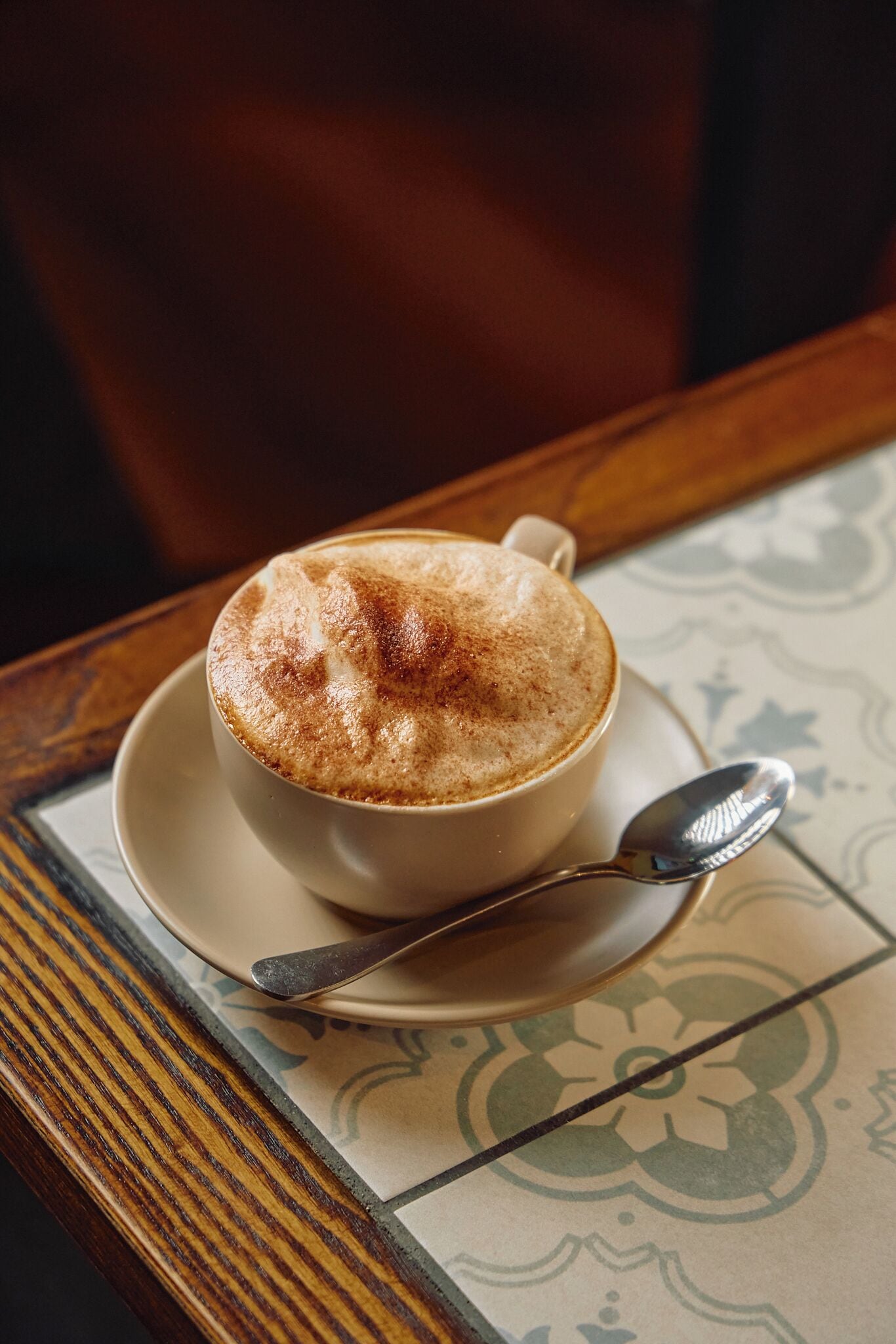 A cup of coffee on a saucer with a spoon, placed on a table with a patterned tablecloth.