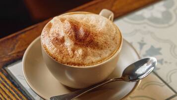 A cup of coffee on a saucer with a spoon, placed on a table with a patterned tablecloth.