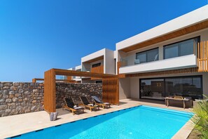 A modern poolside area with lounge chairs, a stone wall, and a wooden pergola. - Aethrion Luxury Villas & Suites (Rhodes)