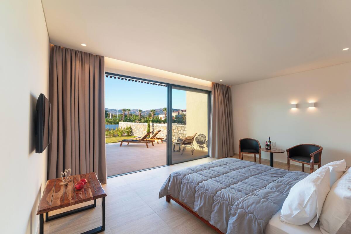 Une chambre d’hôtel moderne dotée d’un grand lit, d’un téléviseur à écran plat, d’une table en bois et d’un balcon avec des chaises et une table.