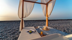 A beachside lounge with a wooden pergola, a table with a magazine, a hat, and a glass of orange juice. - Aethrion Luxury Villas & Suites (Rhodes)