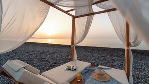 A beachside gazebo with a view of the sunset over the sea, equipped with two lounge chairs and a table with a drink and a hat. - Aethrion Luxury Villas & Suites (Rhodes)