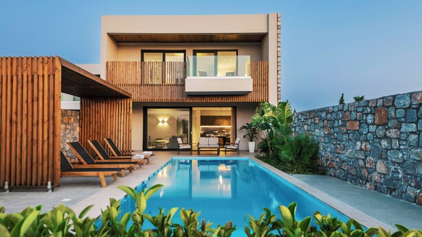 A modern two-story building with a swimming pool, wooden deck, and stone wall. - Aethrion Luxury Villas & Suites (Rhodes)