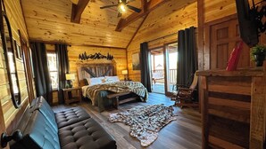 Ein gemütliches Schlafzimmer in einer Blockhütte mit Bett, Bank, Schaukelstuhl und Holzbalkendecke.