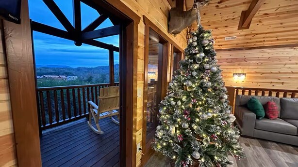 Ein Holzblockhaus-Interieur mit einem geschmückten Weihnachtsbaum, einem Schaukelstuhl und Blick auf die Landschaft.