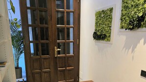 Ein Flur mit einer hölzernen Bank, einer großen Holztür mit Glasfeldern und einer an der Wand befestigten, grünen Pflanze.