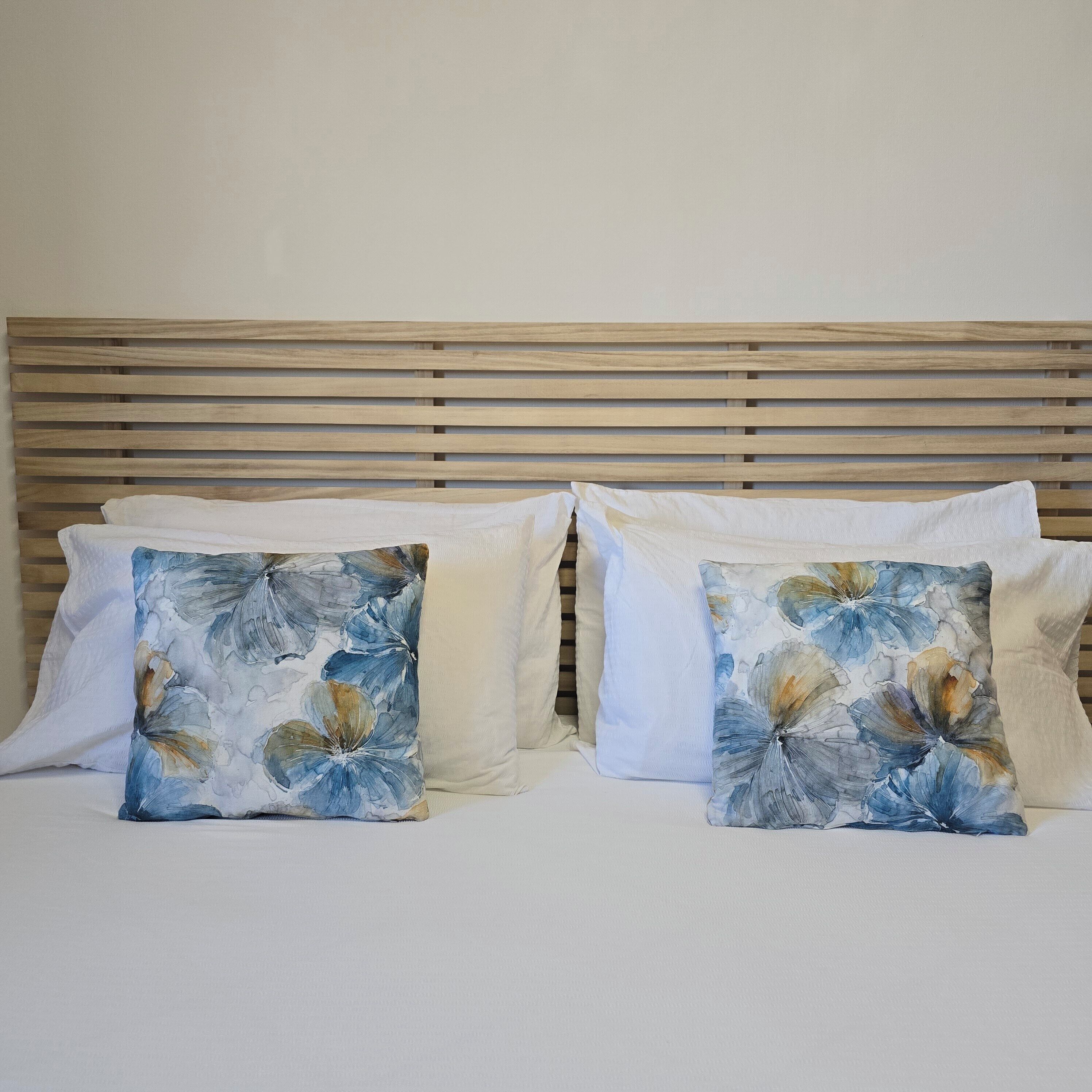 Een bed met een houten hoofdbord en twee sierkussens met een bloemenprint.