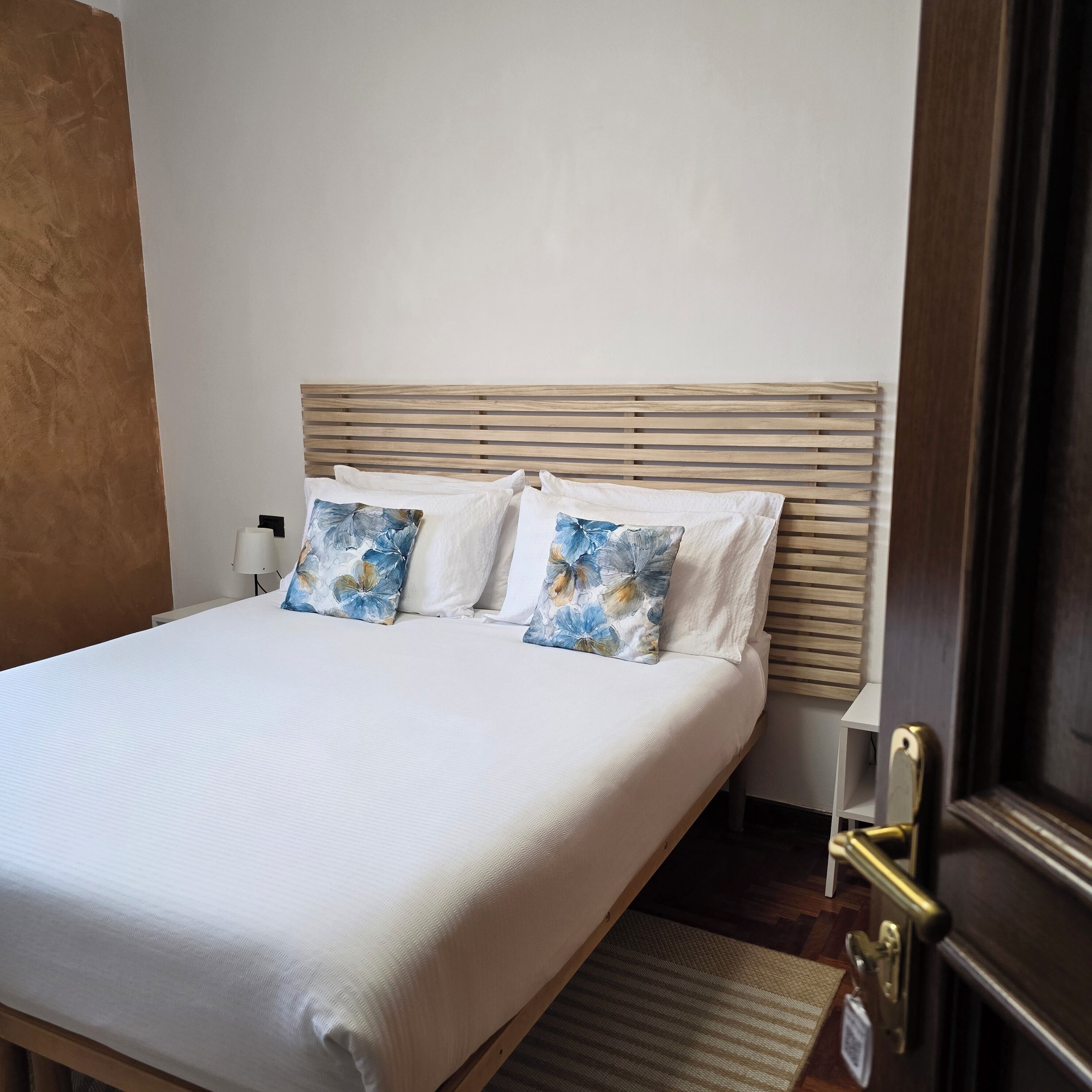 A neatly made bed with a wooden headboard, two pillows with a blue floral pattern, and a white bedspread.
