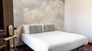 A hotel room with a bed, two pillows, a nightstand, and a wall mural of clouds. - Orio welcome (Grassobbio)
