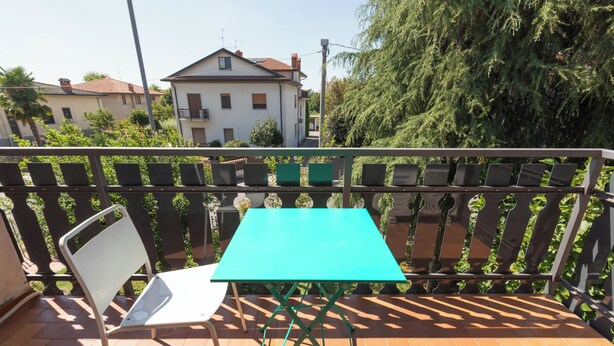 A balcony with a turquoise table and a white chair, surrounded by a metal railing with plants. - Orio welcome (Grassobbio)