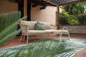 A modern outdoor seating area with a sofa and a small table, surrounded by a tropical leaf-patterned rug. - Orio welcome (Grassobbio)