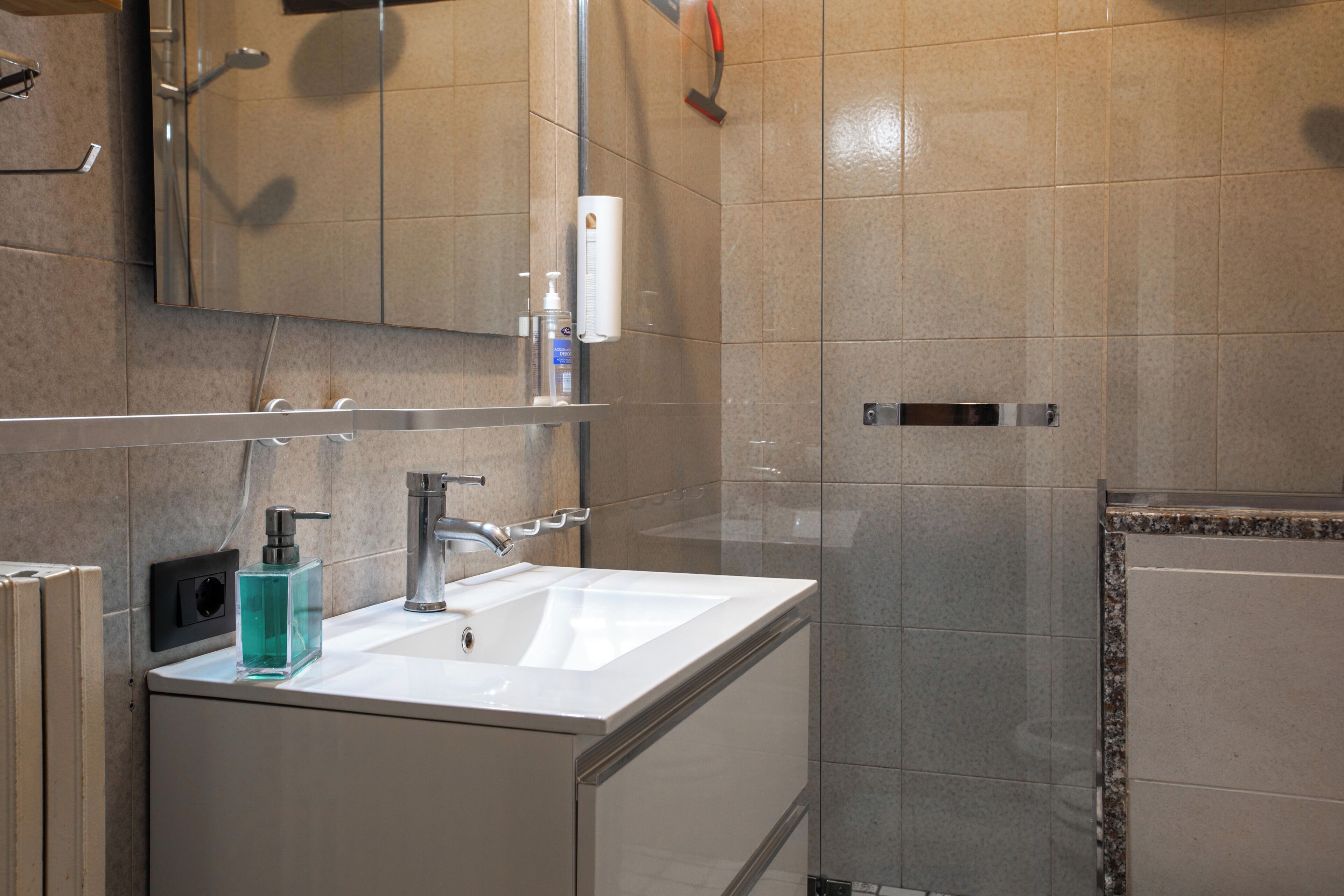 Un baño moderno con un lavabo blanco, un espejo y una zona de ducha.