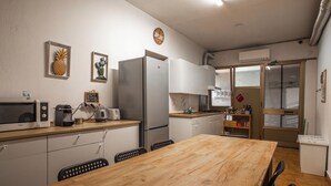 Eine kompakte Küche mit Holztisch, weißen Schränken, einem Kühlschrank, einer Mikrowelle, einem Toaster und einer Wanduhr.