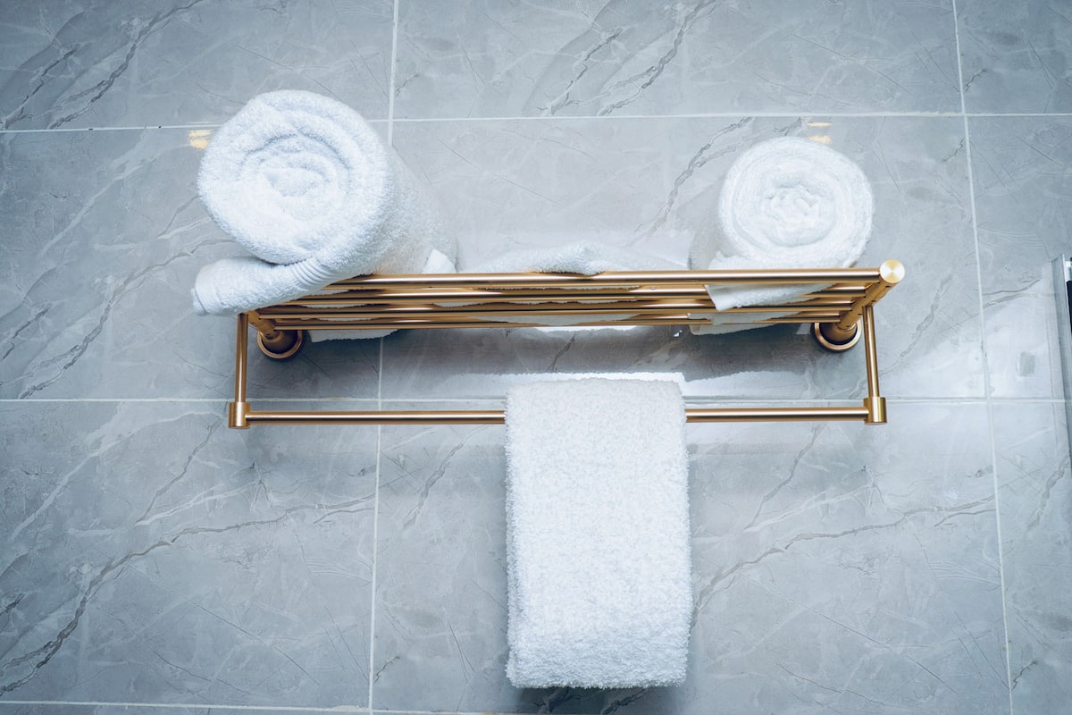 A bathroom with a marble floor, a gold towel rack, and two rolled towels.