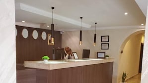 A reception area with a marble floor, wooden reception desk, pendant lighting, and framed certificates on the wall. - Grand Palmac Hotels (Abuja)