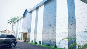 A modern building with a large perforated facade, a parking area, and a few potted plants. - Grand Palmac Hotels (Abuja)
