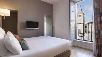 A bedroom with a large window, a bed, a TV, and a lamp.