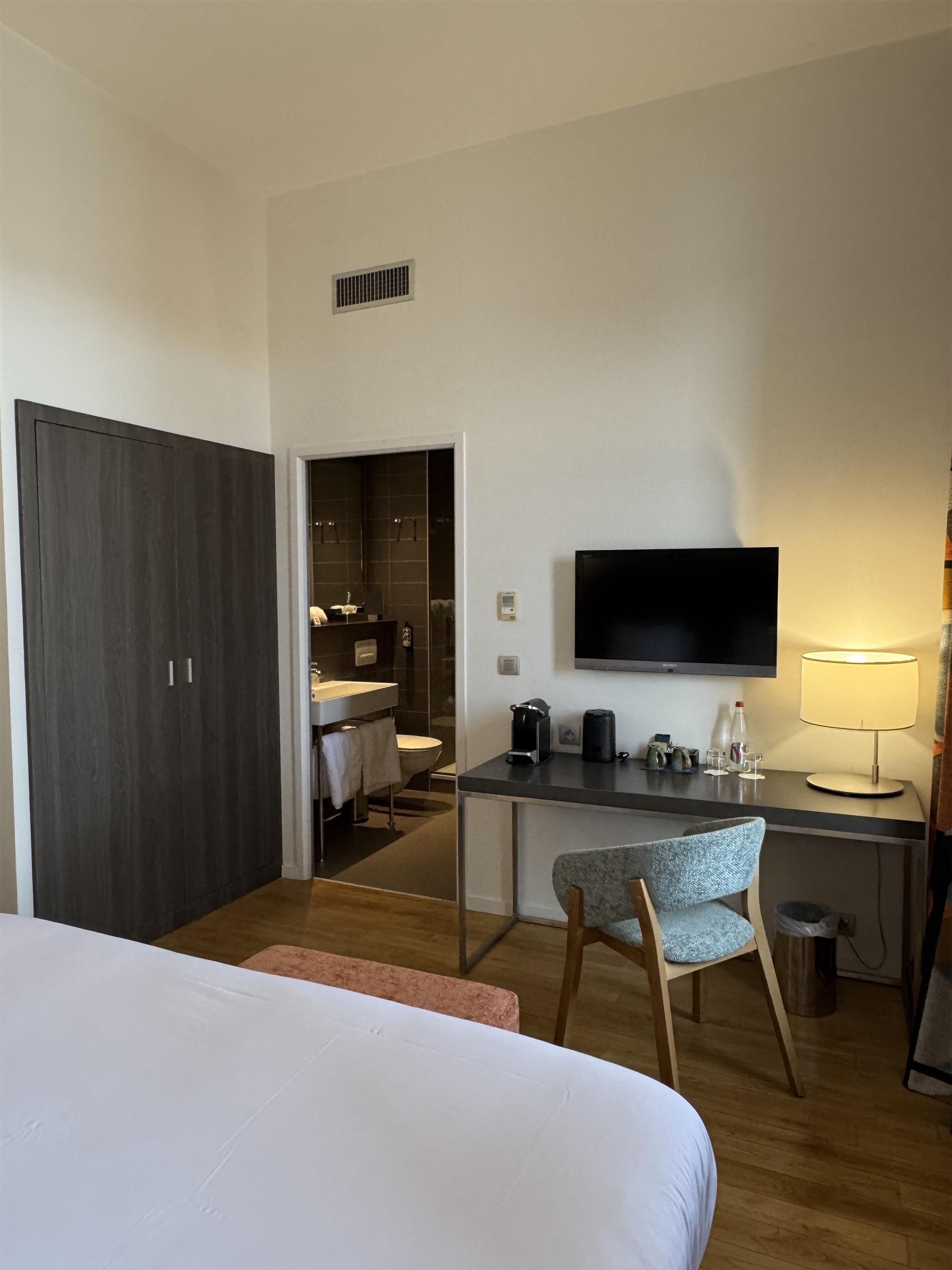 A hotel room with a bed, desk, chair, TV, and a bathroom visible through an open door.