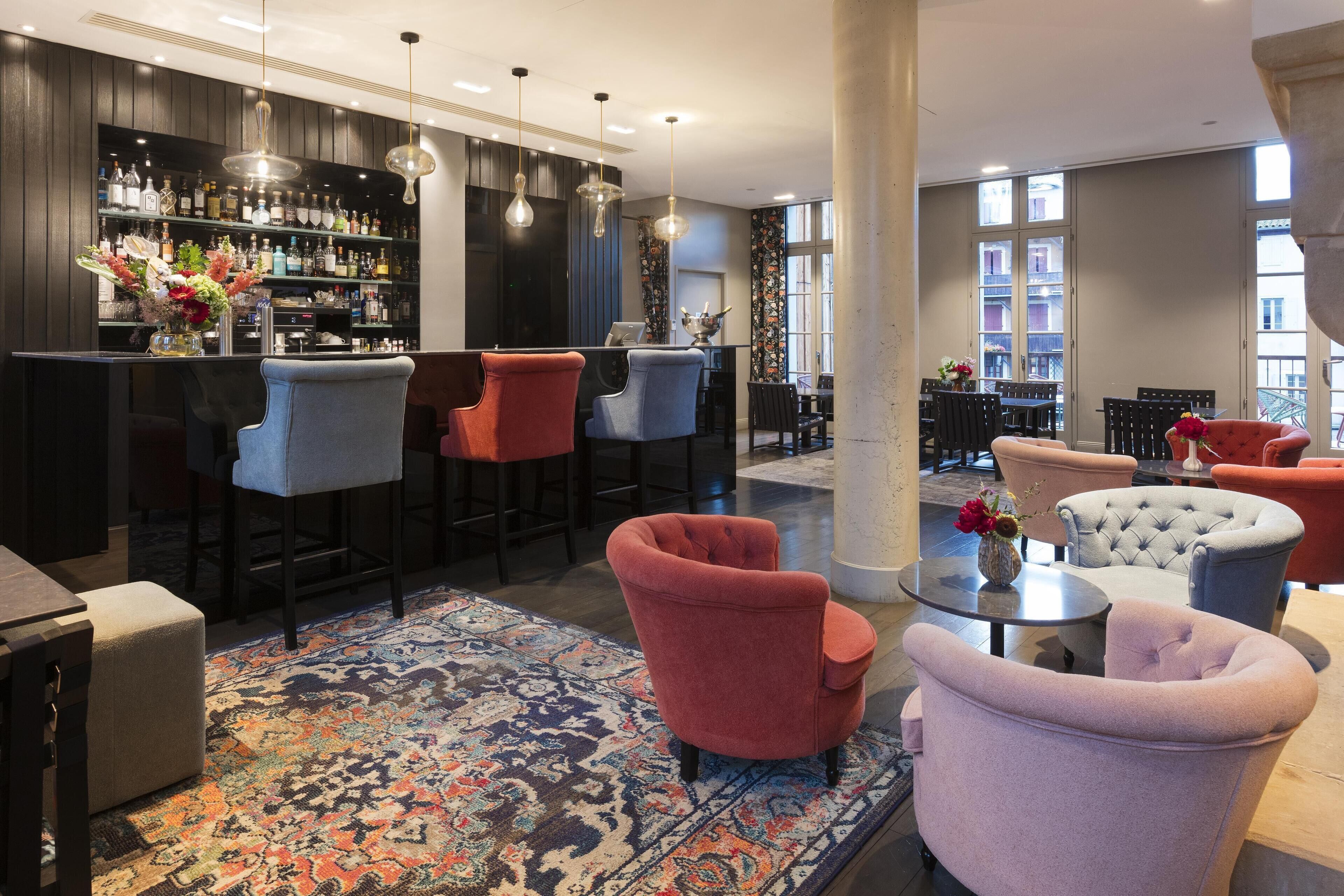 Una zona de bar con varios taburetes, una alfombra estampada y una mezcla de sillones y sofás.