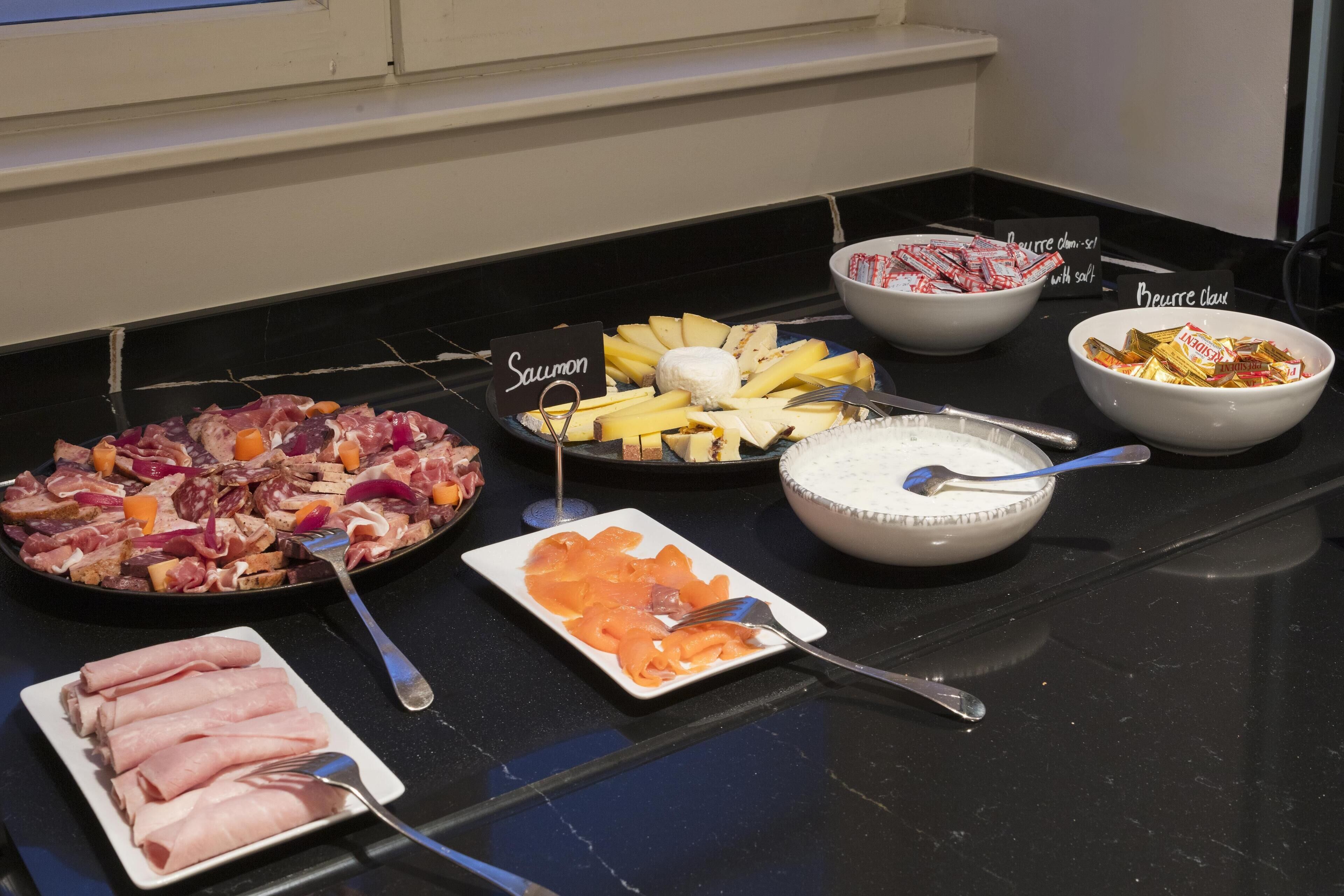 Uma mesa de buffet com diversos alimentos, incluindo salmão, queijo e outras carnes.