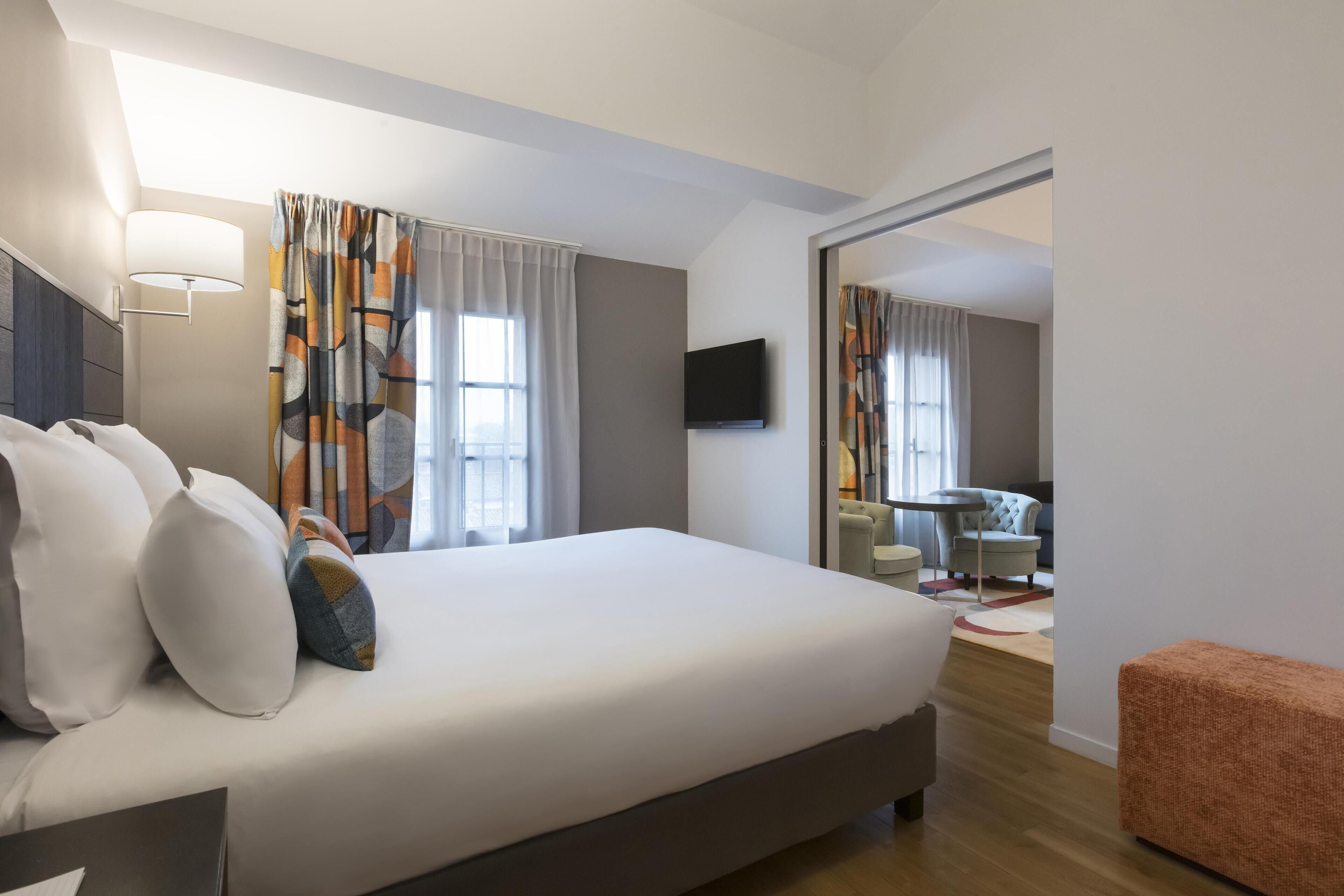 Una habitación de hotel moderna con una cama grande, un televisor de pantalla plana y una zona de estar con una silla y una mesa.