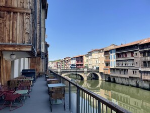 Une terrasse au bord de la rivière, avec des places assises en plein air et une vue sur les bâtiments aux couleurs vives qui se dressent de l’autre côté de l’eau.