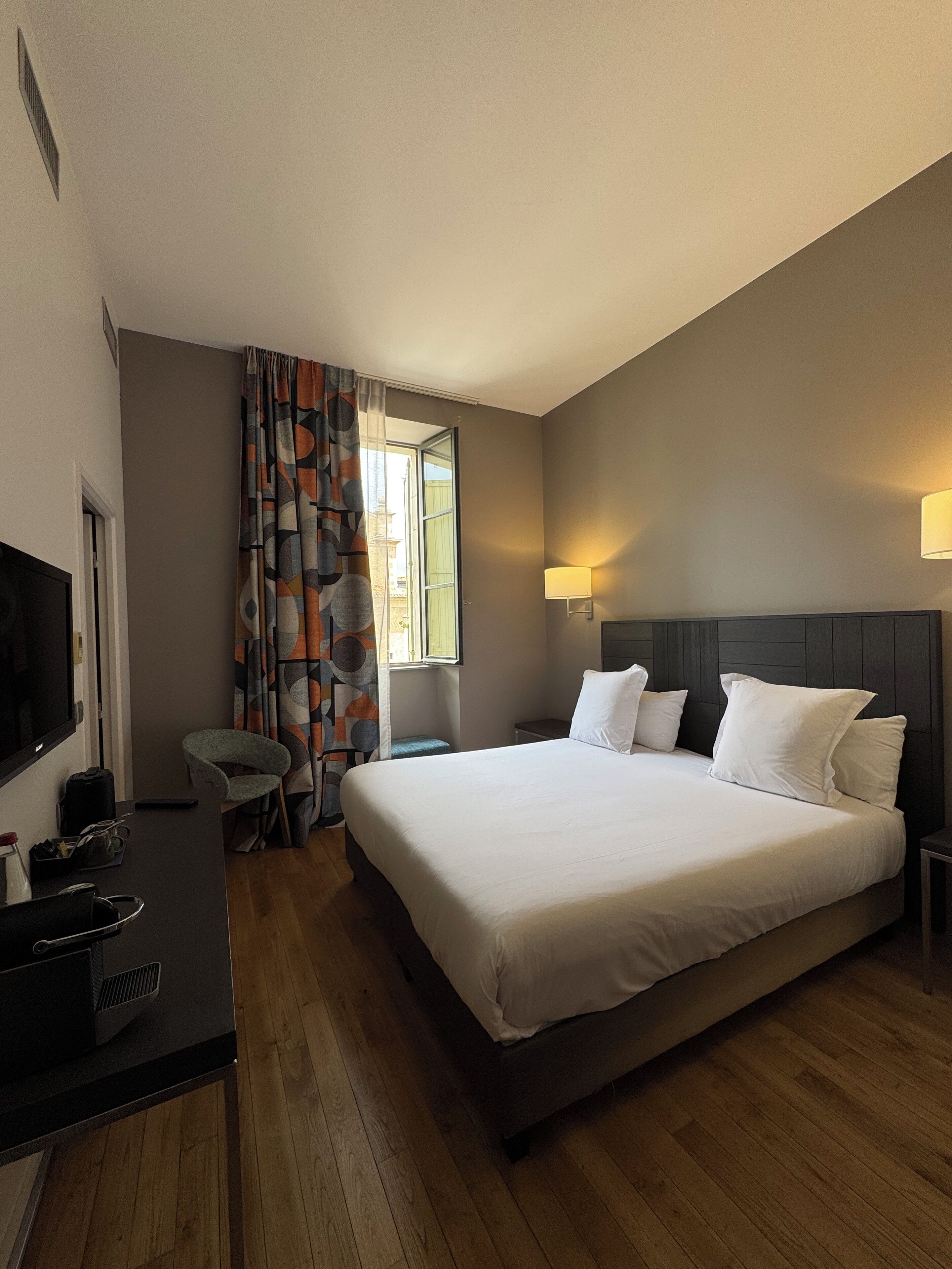 A hotel room with a large bed, a desk with a computer, a chair, and a TV.