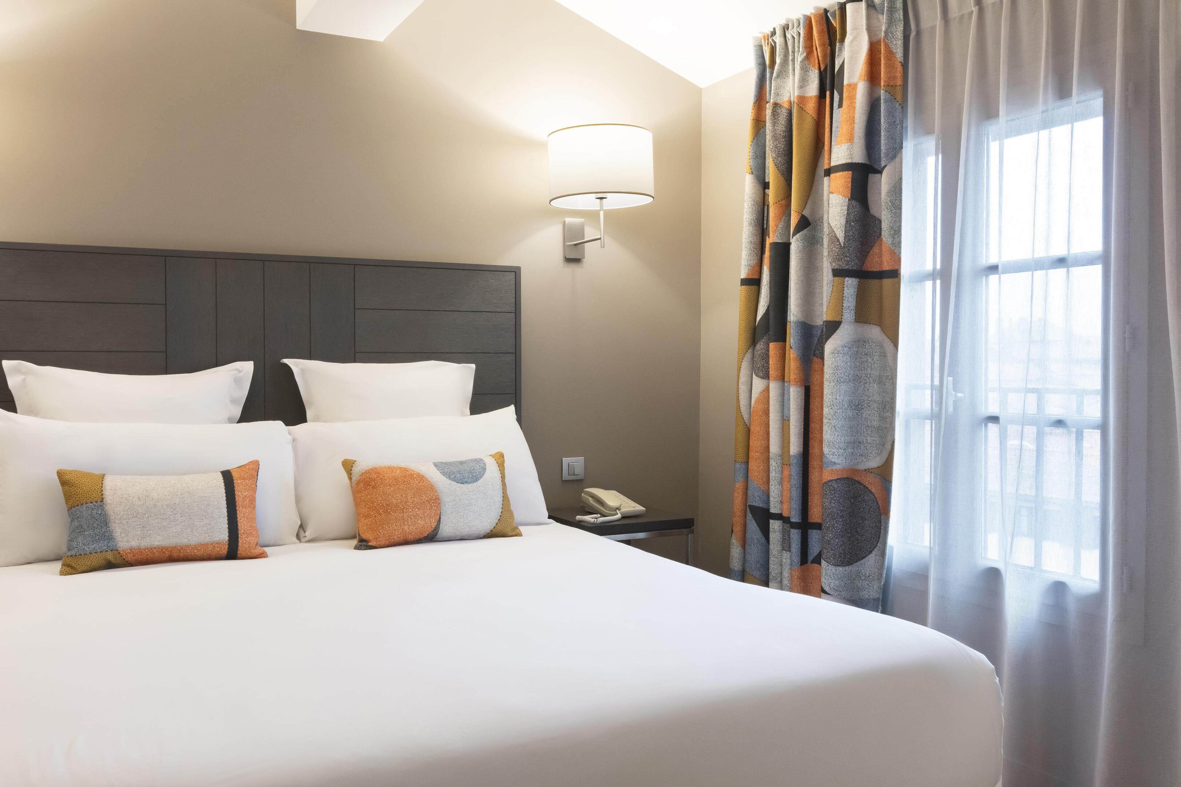 Una camera d'albergo con un letto grande, un comodino con il telefono e una finestra con tende.