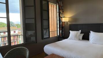 Een hotelkamer met een groot bed, een bureau, een stoel, een raam met uitzicht op gebouwen en een wandlamp.