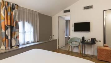 A hotel room with a bed, a television, a small table with a coffee maker, a chair, and a window with curtains.